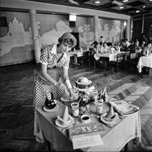 Официантка в образе Красной шапочки сервирует стол | Общепит. 1983 г., г.Северодвинск. Фото #C2266.